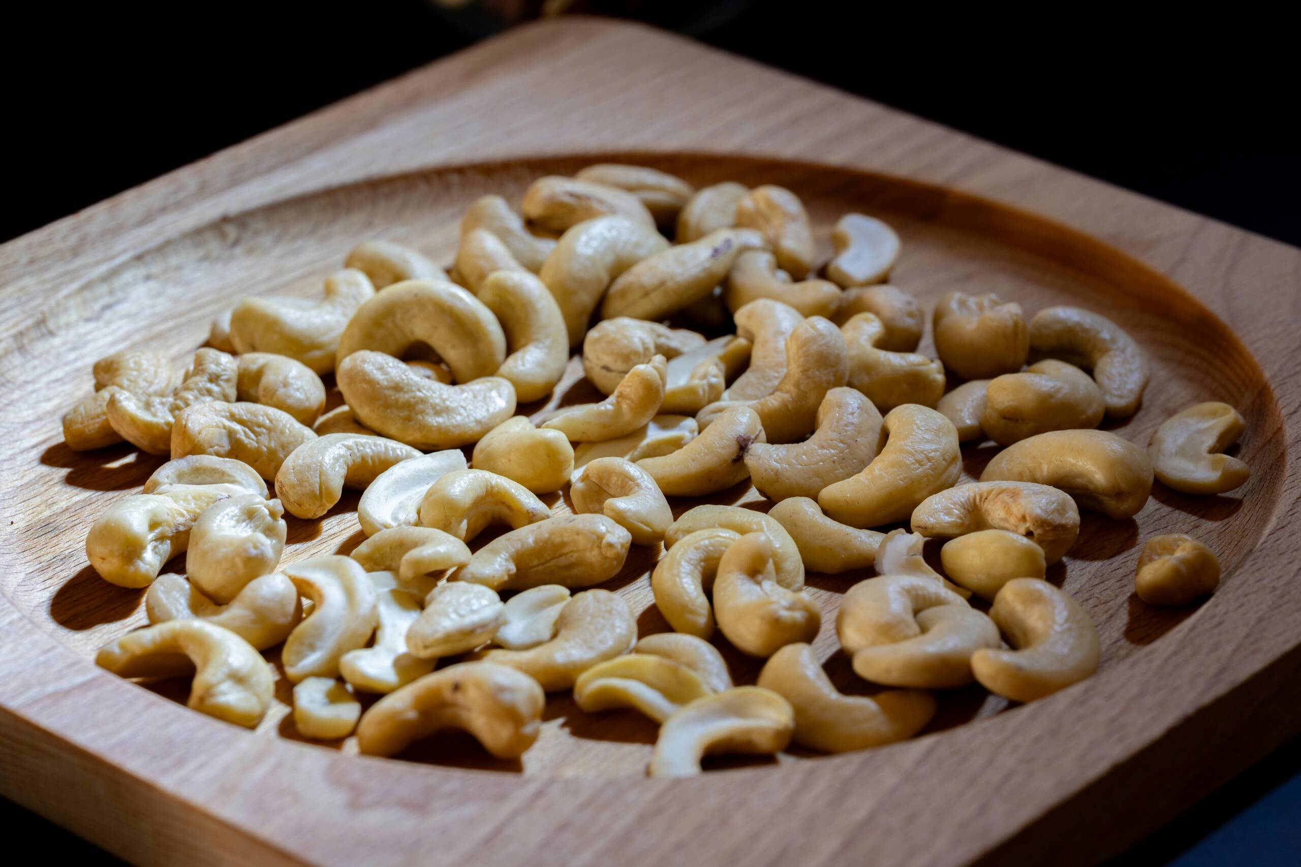 Delicious raw cashews on a wooden board, perfect for healthy snacking or cooking.