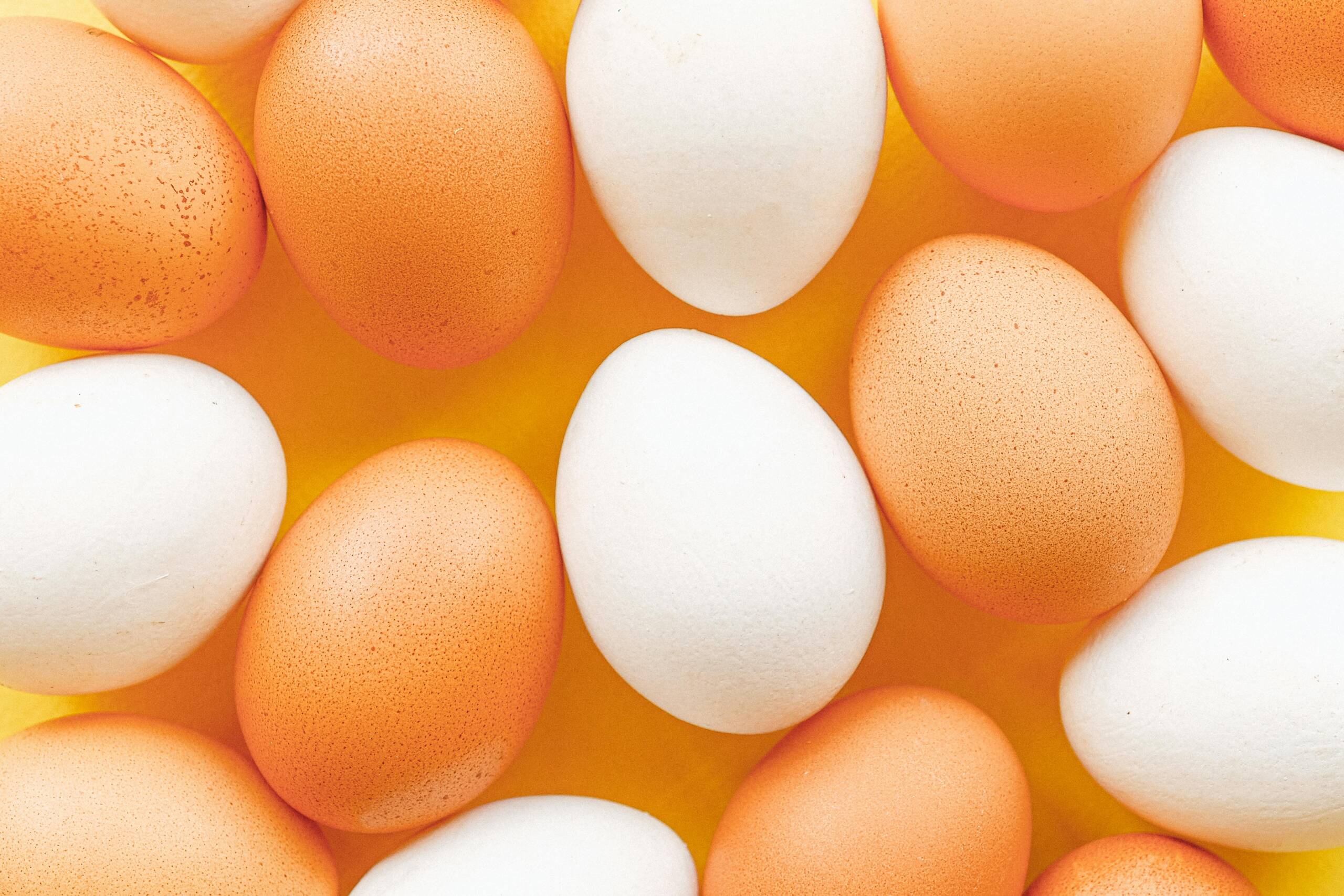 Top view of brown and white eggs arranged on a vibrant yellow surface, offering a minimalistic food pattern.