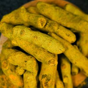 Vibrant close-up of organic turmeric roots displayed on a wooden plate, perfect for cooking and health inspiration.